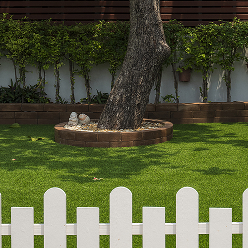 Selective focus at large tree trunk and row of green bush plant on artificial turf in front yard of home with blurred white wooden fence on foreground, home gardening and exterior architecture concept